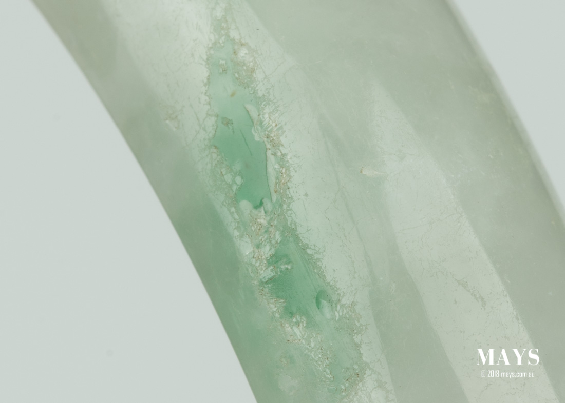 The photo shows an area of a Type B Jade Bangle where the polymer on the surface has started to degrade revealing the corrosion it once use to conceal.